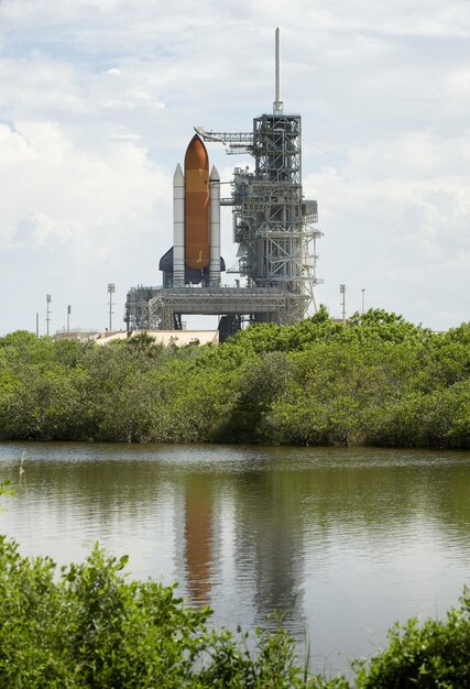 A panoramic view of the Kennedy Space Center in Florida, with a massive rocket standing tall against the clear blue sky. Visitors are seen gazing in awe at the spacecraft, and the overall scene conveys a sense of technological marvel and space exploration.