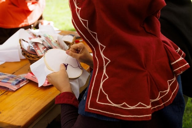 A beginner cosplayer working on a simple costume design on a table scattered with fabrics, patterns, and sewing tools. The background is a cluttered but organized crafting room with shelves of materials.