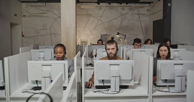 A brightly lit room filled with computer equipment, monitors displaying code, and people working collaboratively on a software development project. Whiteboards covered in diagrams and notes are visible in the background.