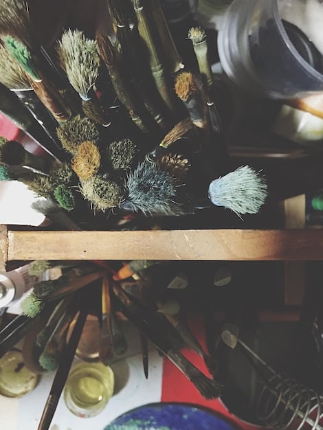 A well-organized workspace with various miniature painting tools and materials. The image includes a selection of acrylic paints, different sized brushes, a wet palette, primed miniatures, hobby knife, and a magnifying glass. The lighting should be bright and focused, highlighting the tools and materials.