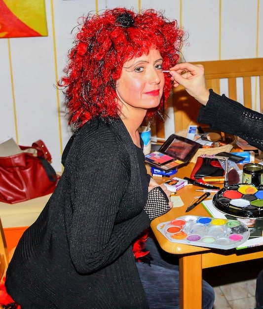 A cosplayer demonstrating advanced makeup techniques, with various brushes and palettes spread out on a table.