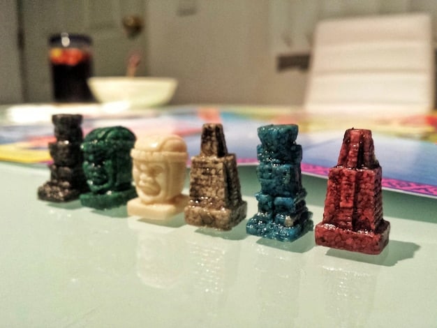 A close-up shot of a variety of modern board game components, including intricately designed miniatures, colorful dice, uniquely illustrated cards, and wooden tokens. Focus is on the textures and details of the pieces, highlighting the craftsmanship.