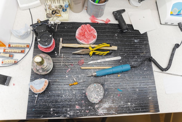 A detailed, well-lit workspace filled with various crafting materials like foam sheets, paints, sculpting tools, and molds. A half-finished prop weapon sits in the center, showcasing the layers and techniques used in its construction.