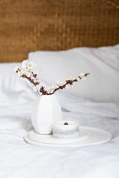 A bedroom interior in the US featuring a low wooden bed frame, linen bedding in neutral colors, a bamboo screen, and a ceramic vase with a single branch, all inspired by Korean natural aesthetics.