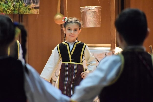 A group of people, including children, participate in a Hanbok-making workshop at a Korean Cultural Center. They are enthusiastically cutting fabric and sewing, guided by instructors. The atmosphere is lively and educational, emphasizing the hands-on learning experience of traditional Korean crafts.