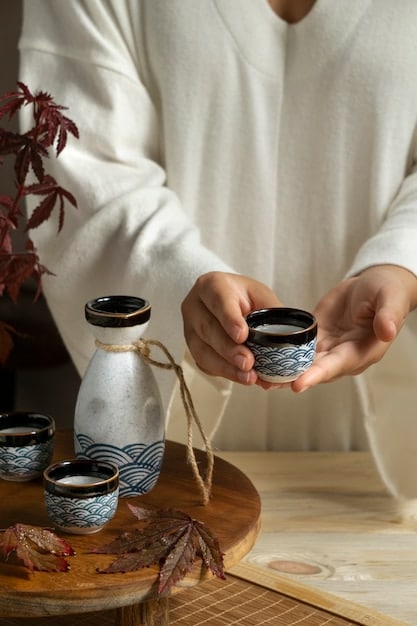 A person respectfully holding a teacup with both hands during a Korean tea ceremony. The person is dressed in traditional Korean clothing, and the background is softly blurred.