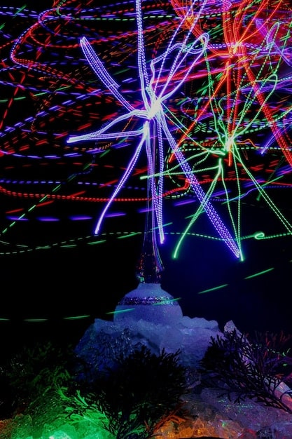A close-up shot of K-Pop light sticks waving in unison during a concert, creating a sea of colorful lights. The focus is on the intricate designs and vibrant colors of the light sticks.