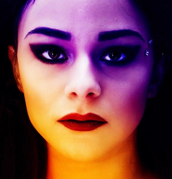 A close-up shot of a K-Pop artist's face, showcasing vibrant makeup and expressive eyes. The lighting highlights the artist's features, drawing the viewer's attention to their emotion and performance.