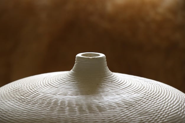 A close-up shot of a modern lamp designed with a Korean pottery-inspired shape. The lamp is made of white ceramic and has a minimalist wooden base. Soft, warm light emanates from the lamp, highlighting its organic curves and subtle texture.