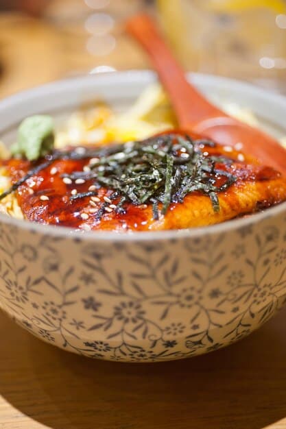 A close-up of a bowl of bibimbap topped with various colorful vegetables, gochujang sauce, a fried egg, and garnished with sesame seeds in a rustic, yet modern, setting.