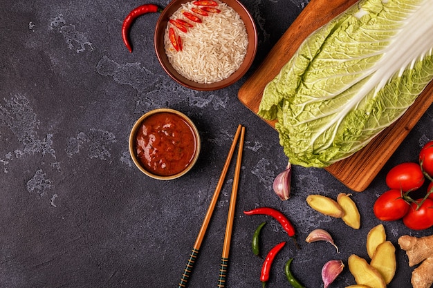 A top-down shot of various kimchi ingredients laid out on a wooden surface, including napa cabbage, Korean chili flakes (gochugaru), garlic, ginger, fish sauce, and scallions, arranged neatly to showcase their vibrant colors and textures.