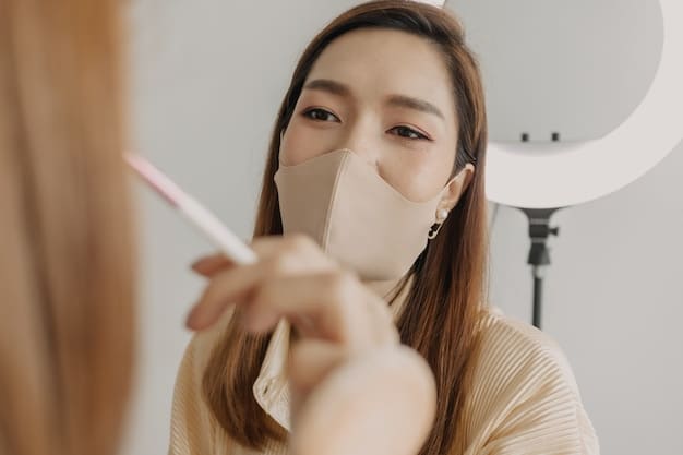 Close-up of a Korean beauty influencer applying a sheet mask on her face while recording a video tutorial. The background is a well-lit, minimalist home studio setting with Korean beauty products neatly arranged on a shelf.