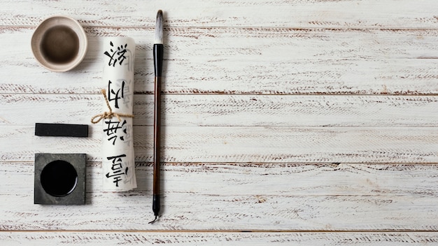 A traditional Korean calligraphy set is arranged artfully on a wooden table. It includes brushes of varying sizes, an inkstone with a partially ground inkstick, a ceramic water dropper, and several sheets of Hanji paper. The overall scene is bathed in soft, natural light, highlighting the textures and colors of the materials.