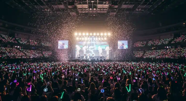 Energetic K-Pop concert crowd with lightsticks and idols performing on stage.