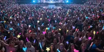 K-Pop fans enthusiastically chanting at a live concert with lightsticks